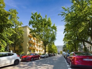 A street lined with parked cars and trees, with buildings on either side.