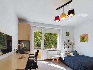 Una habitación moderna y bien iluminada con un ventanal grande, una cama, un escritorio y una silla.