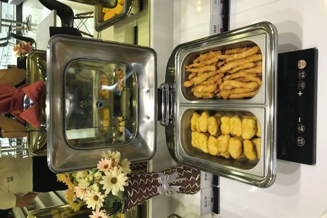 A buffet with two trays of food, one with breaded items and the other with fried items, and a decorative vase with flowers.