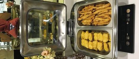 A buffet with two trays of food, one with breaded items and the other with fried items, and a decorative vase with flowers.