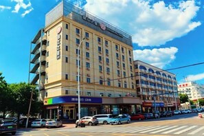 A multi-story hotel with a prominent sign, several ground-level shops, and a parking lot with cars. - Jinjiang Inn Select Hotel (Tianjin Tanggu Subway Station Zhongxin North Road) (Tianjin)