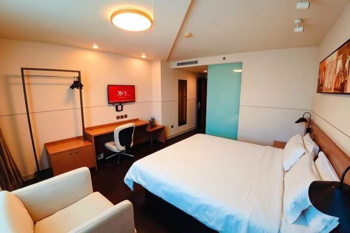 A hotel room with a bed, a desk, a chair, a wardrobe, and a TV.