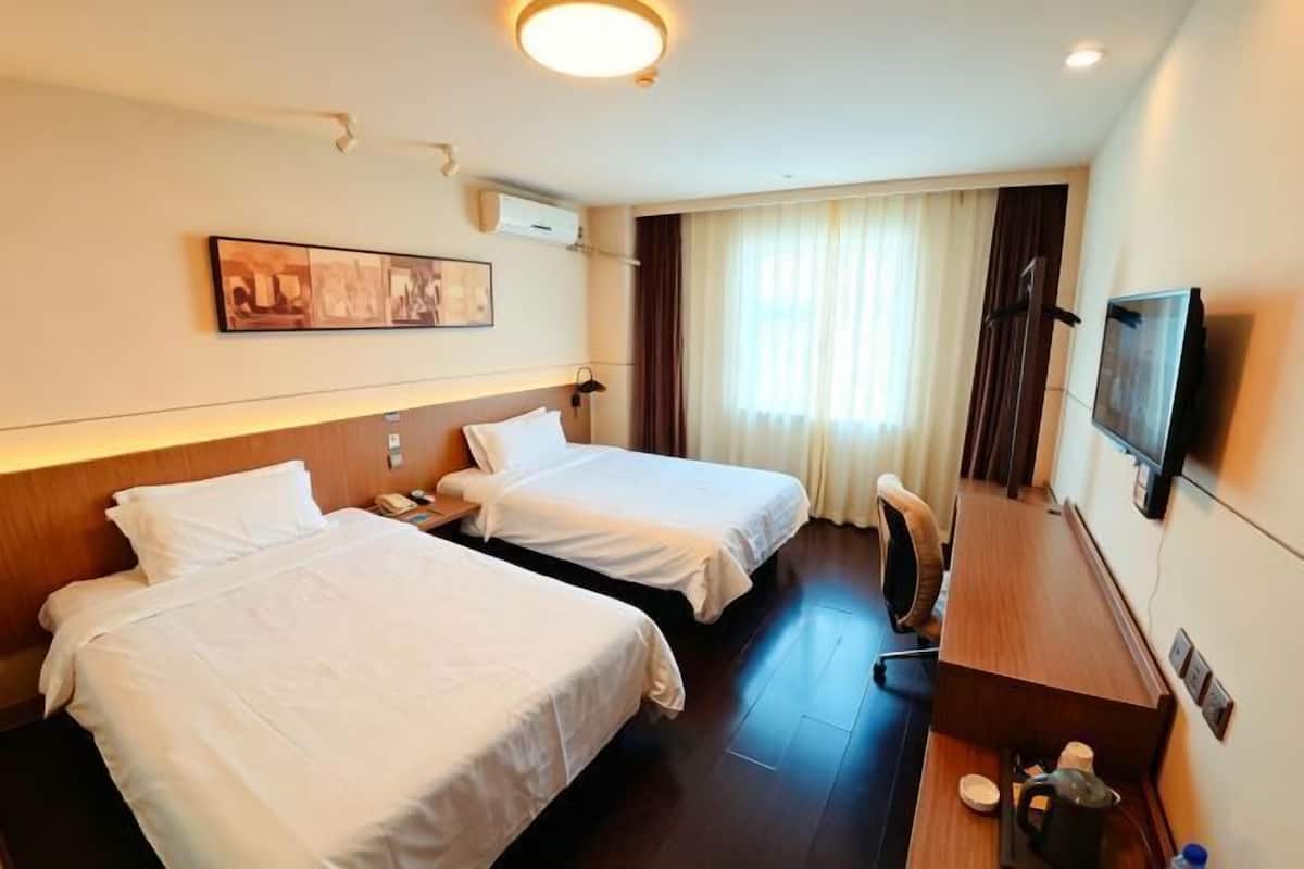 A hotel room with two beds, a desk, a chair, a television, and a window with curtains.