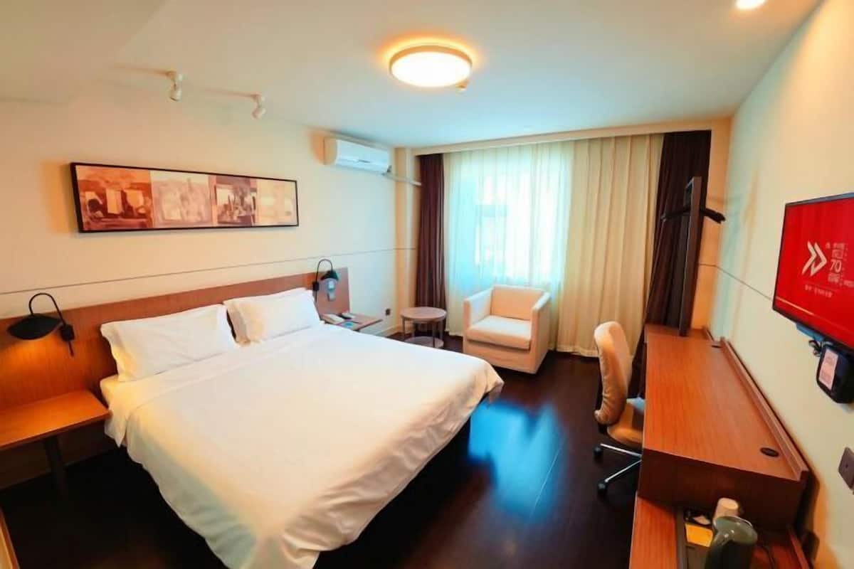 A hotel room with a bed, a desk, a chair, a television, and a painting on the wall.