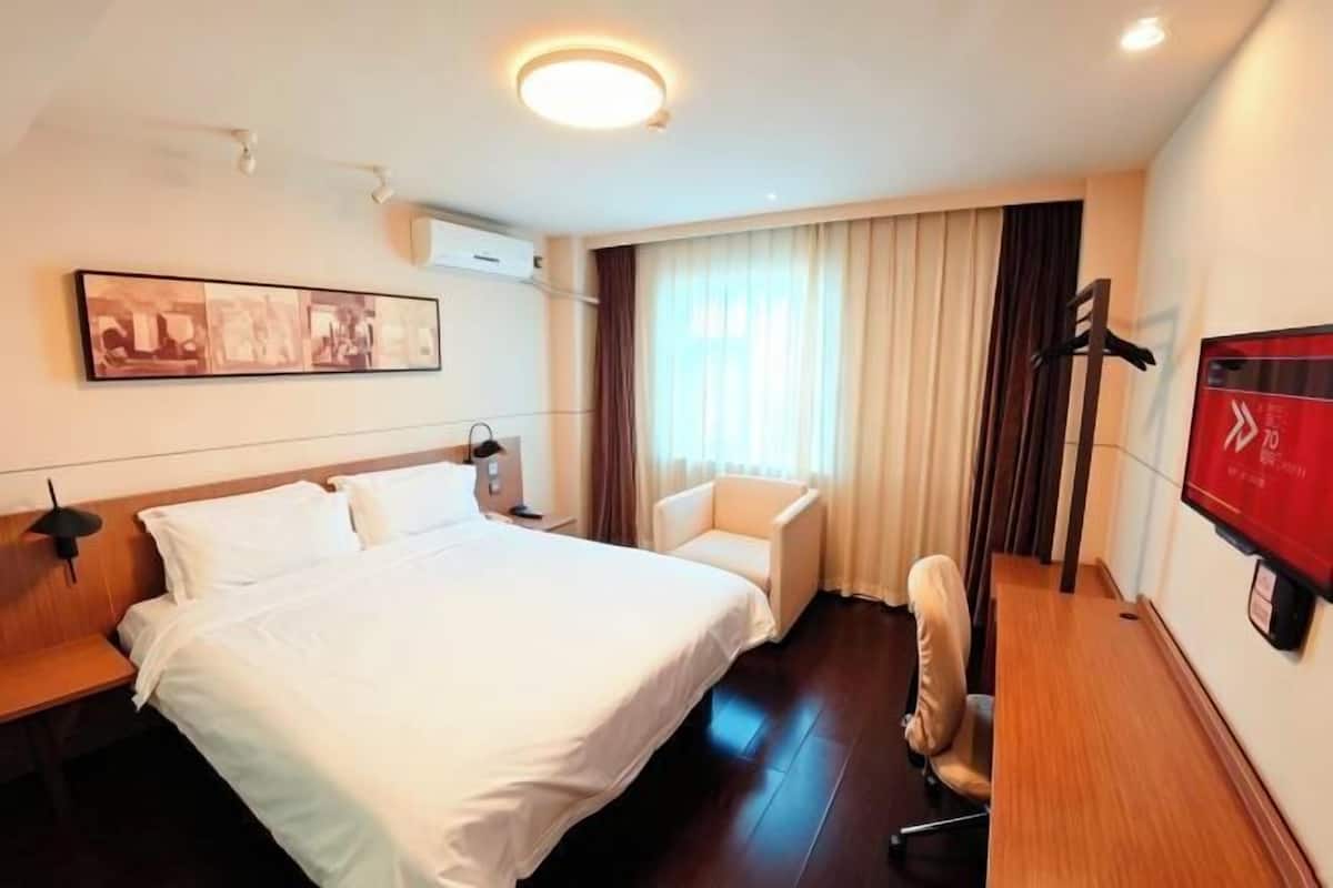 A hotel room with a large bed, a desk, a chair, a TV, and a window with curtains.