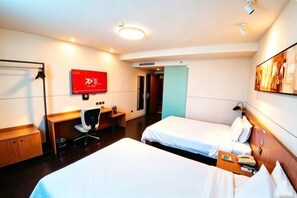A hotel room with two beds, a desk, a chair, a TV, and a door.