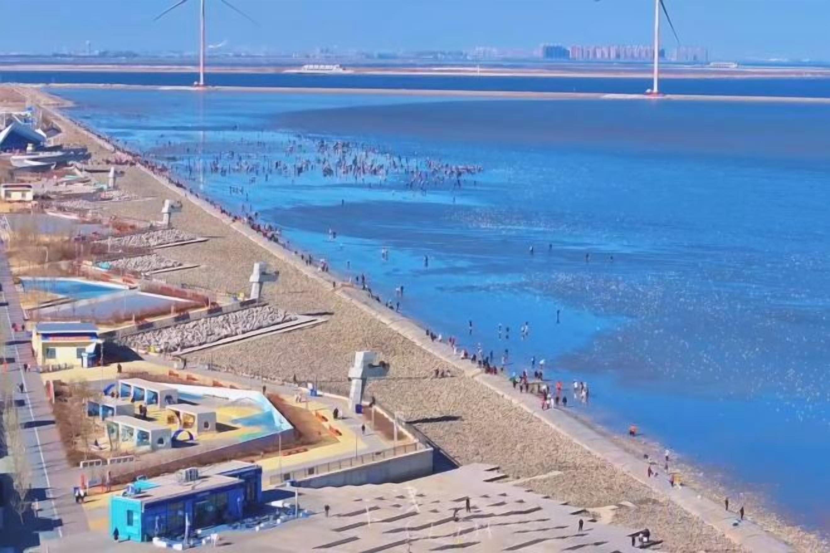 A coastal area with a beach, a pier, and a building with a blue roof.