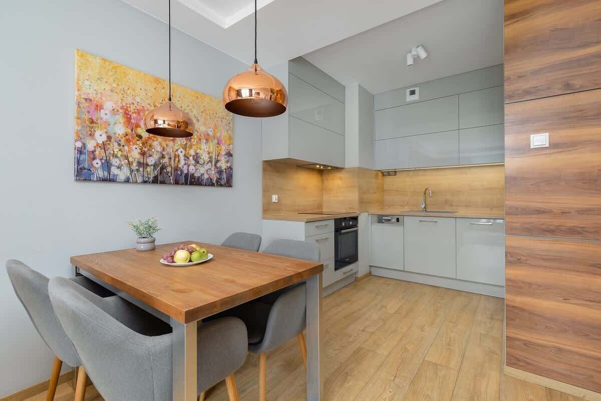 A modern kitchen with a wooden dining table, grey chairs, and a large painting on the wall.