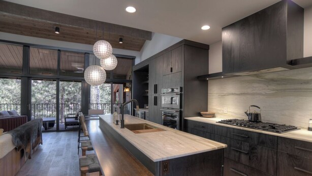 A modern kitchen with dark wood cabinets, a marble countertop, and a large island with seating. - Lenny's Lair | AC, Pool, Hot Tub, Golf & Ski (Durango)