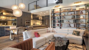 A modern living room with a sectional sofa, a coffee table, and a dining area with a kitchen in the background. - Lenny's Lair | AC, Pool, Hot Tub, Golf & Ski (Durango)