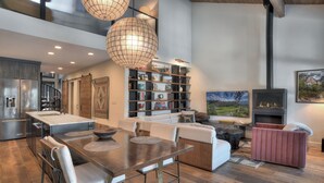 A modern kitchen with a built-in oven, a dining area with a wooden table and chairs, a bookshelf, and a fireplace. - Lenny's Lair | AC, Pool, Hot Tub, Golf & Ski (Durango)
