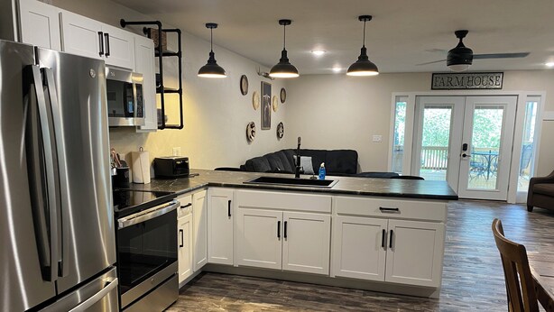 A modern kitchen with stainless steel appliances, white cabinetry, and a farmhouse sign.