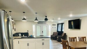 A spacious kitchen with a central island, a dining area with a wooden table and chairs, and a TV mounted on the wall.