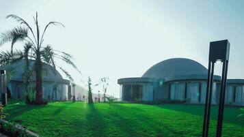 A large, modern building with a dome structure, surrounded by well-maintained grass and palm trees.