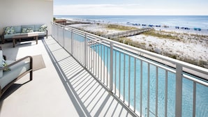 A balcony with a pool, a sofa, and a view of the beach and ocean.