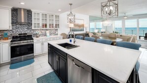 A modern kitchen with a large island, stainless steel appliances, and a view to the ocean.