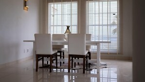A dining area with a white table and chairs, a vase on the table, and a window with blinds. - Artiko Luxury Suites - Jan Thiel (Jan Thiel)