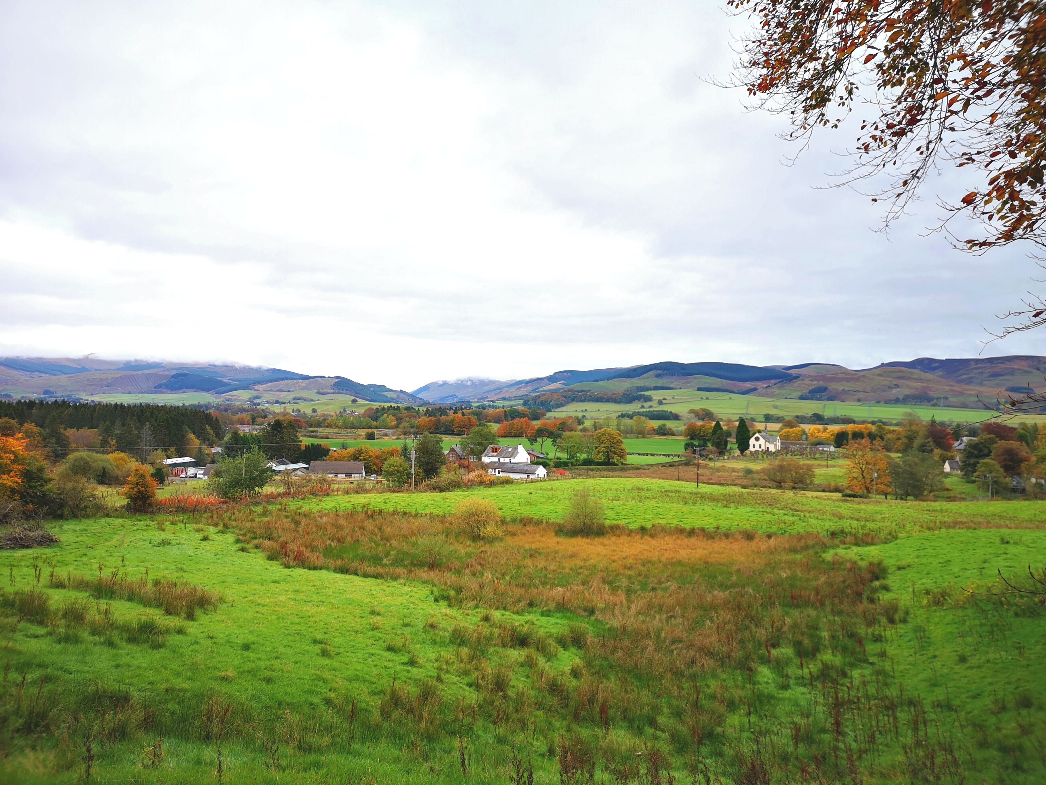 Un paisaje rural con colinas ondulantes, algunas casas y cielo despejado.