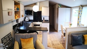 Une cuisine moderne dotée d’un îlot central, un coin repas avec une table et des chaises, et un espace salon confortable avec un canapé et un fauteuil.