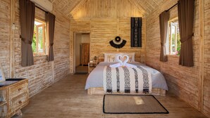 A wooden cabin-style bedroom with a bed, curtains, a wall hanging, and a small bedside table. - Bale Taru Pecatu  (Pecatu)