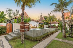 A resort with a pool, palm trees, and a signpost with directions to various amenities. - Bale Taru Pecatu (Pecatu)