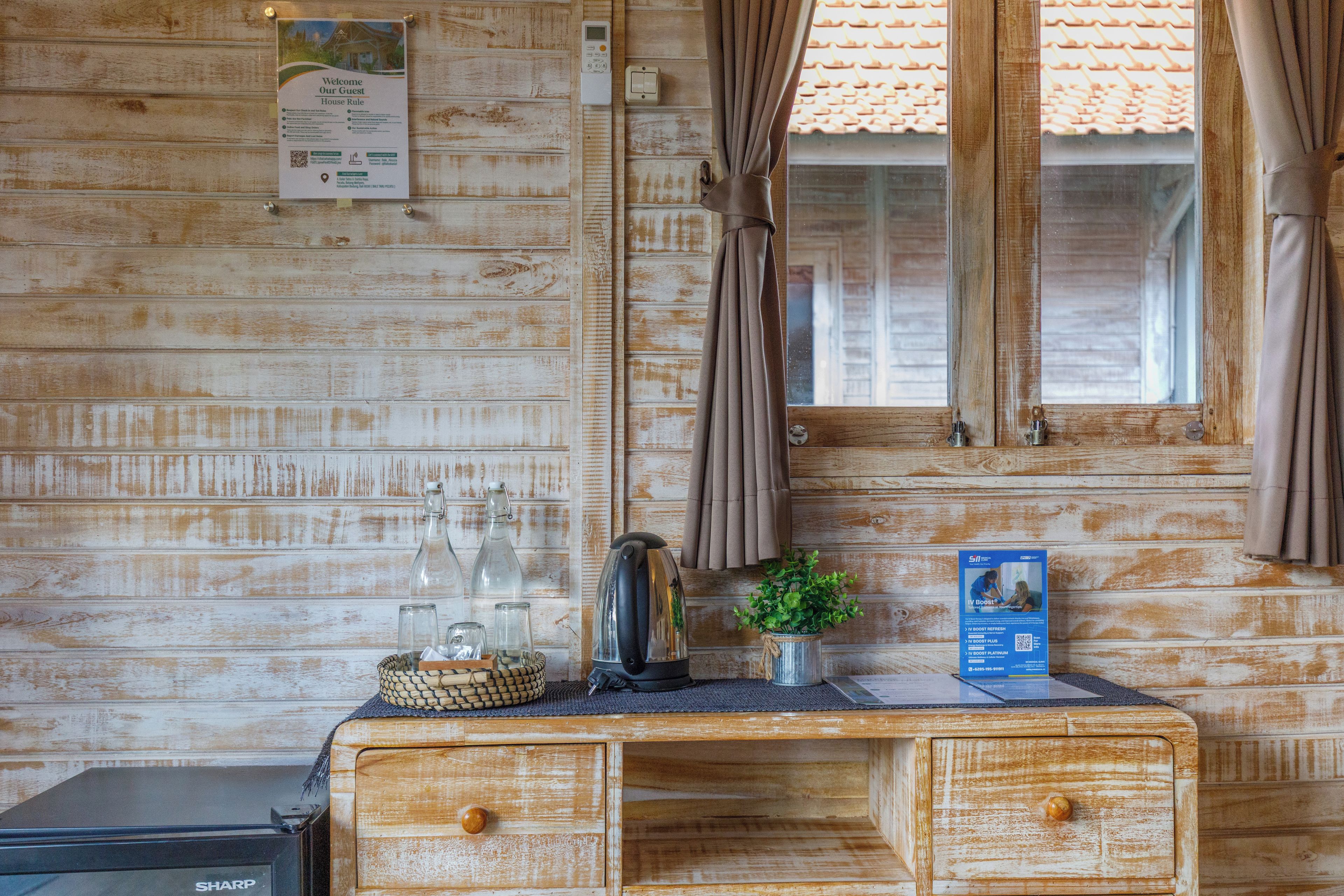 Ein Holzhütten-Interieur mit einem Schreibtisch, einem Wasserkocher, einer Glasflasche, einer kleinen Pflanze und einem Poster an der Wand.