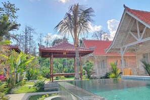 A traditional wooden building with a red tiled roof, a covered seating area, and a pool. - Bale Taru Pecatu (Pecatu)