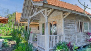 A rustic wooden house with a tiled roof, a porch, and a garden with various plants. - Bale Taru Pecatu  (Pecatu)
