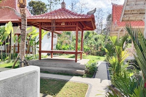 A traditional wooden gazebo with a tiled roof, surrounded by lush greenery and a well-maintained garden. - Bale Taru Pecatu (Pecatu)