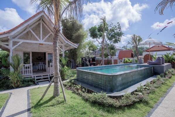 A pool area with a wooden structure, palm trees, and a clear sky. - Bale Taru Pecatu (Pecatu)