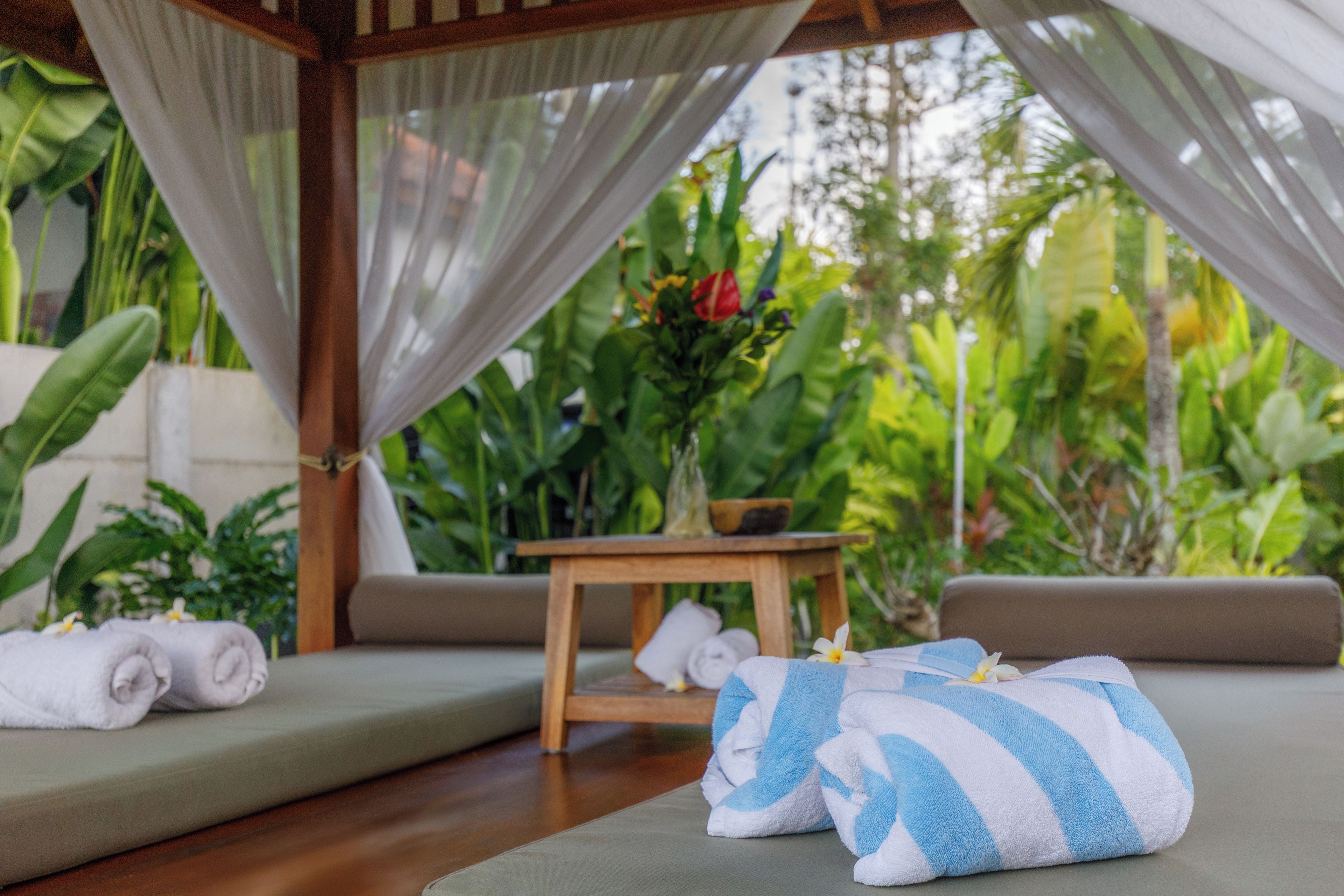 A serene outdoor seating area with a wooden table, cushions, and towels.