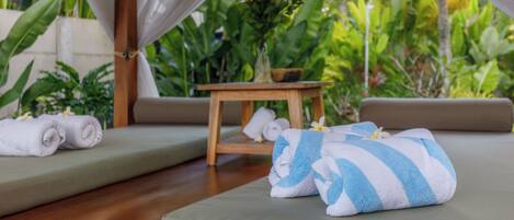 A serene outdoor seating area with a wooden table, cushions, and towels.