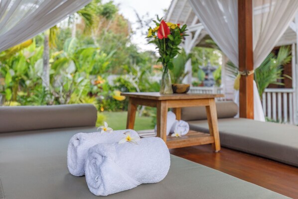 A spa area with a wooden table, two towels, and a vase of flowers. - Bale Taru Pecatu (Pecatu)