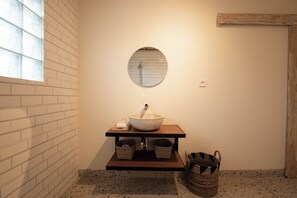 A bathroom with a round mirror, a vessel sink, and two baskets on a wooden shelf. - Bale Taru Pecatu (Pecatu)