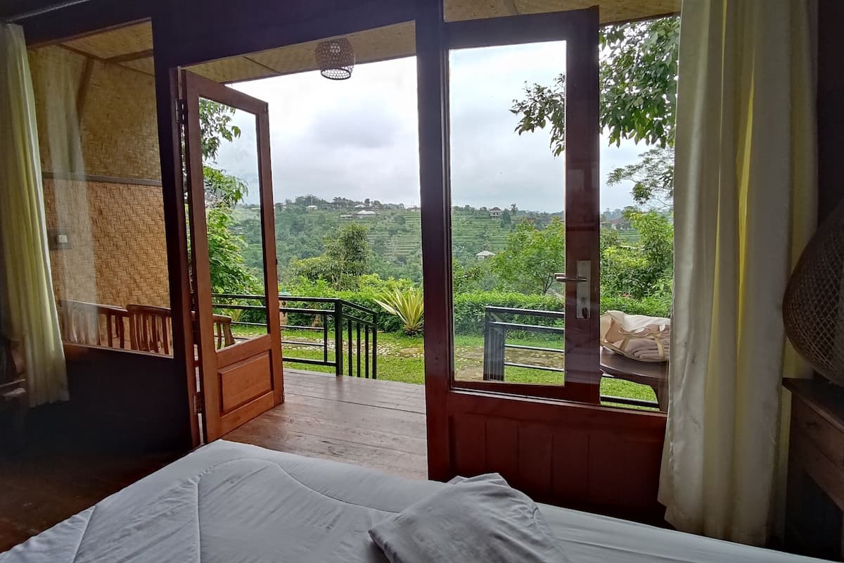Una habitación con cama, puerta de madera y vista a un paisaje verde.