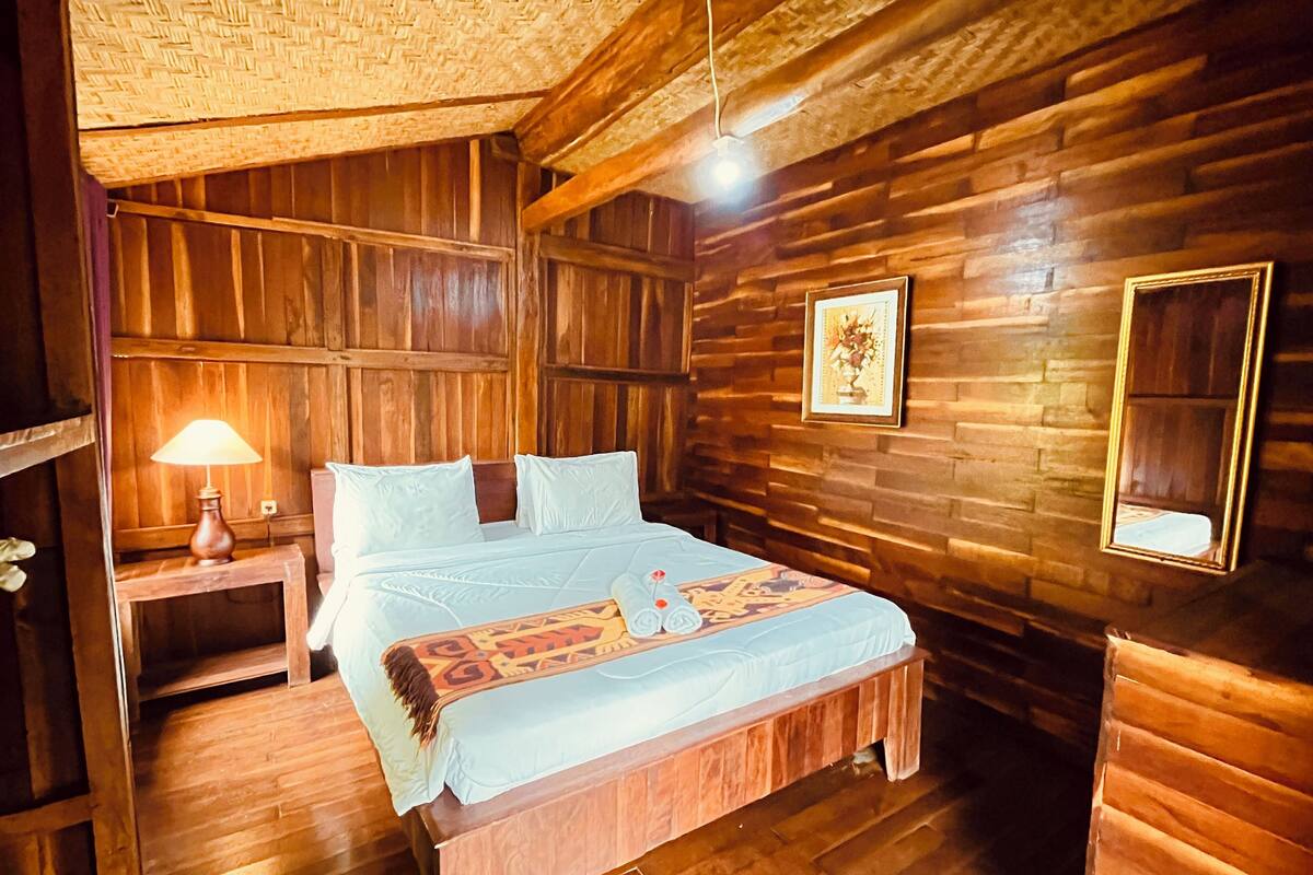 Una habitación de madera con una cama, una mesita de noche, una lámpara y un cuadro en la pared.