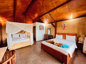 Una habitación con dos camas, una con dosel y otra sin, un banco de madera, una mesita y un espejo en la pared.