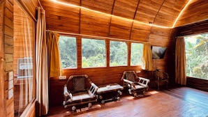 Una baita in legno con soffitto alto, due zone relax con cuscini e un televisore montato a parete.