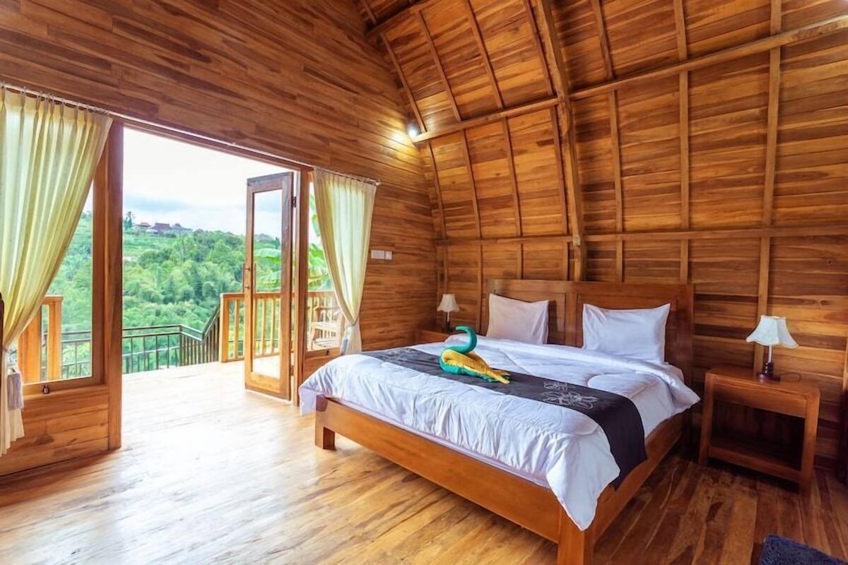 Una habitación de madera con cama, mesitas de noche y balcón con vista a la vegetación.