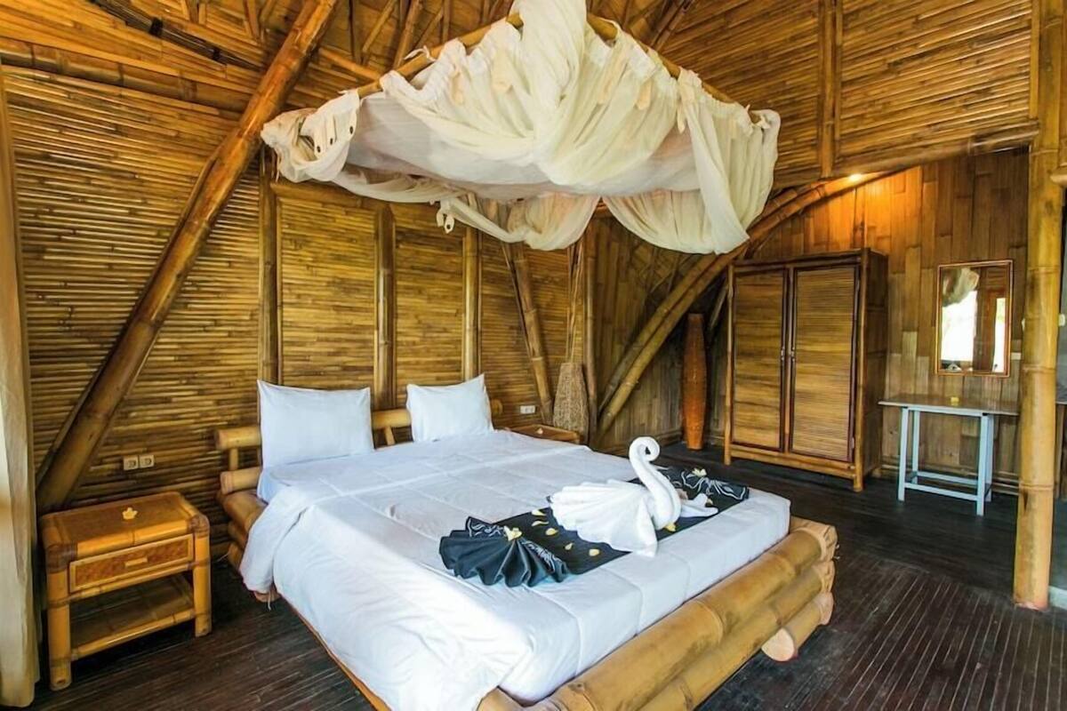 Una habitación con cama, mesita de noche, espejo y dosel.