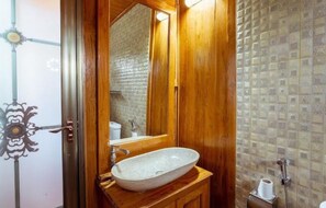 Un baño de madera con un lavamanos ovalado grande, un espejo y una zona de ducha.