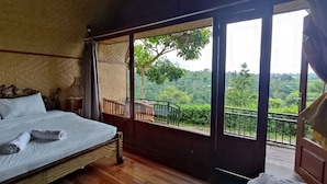 Camera da letto con un letto grande, pavimento in legno, un balcone con ringhiera e vista su un paesaggio rigoglioso.
