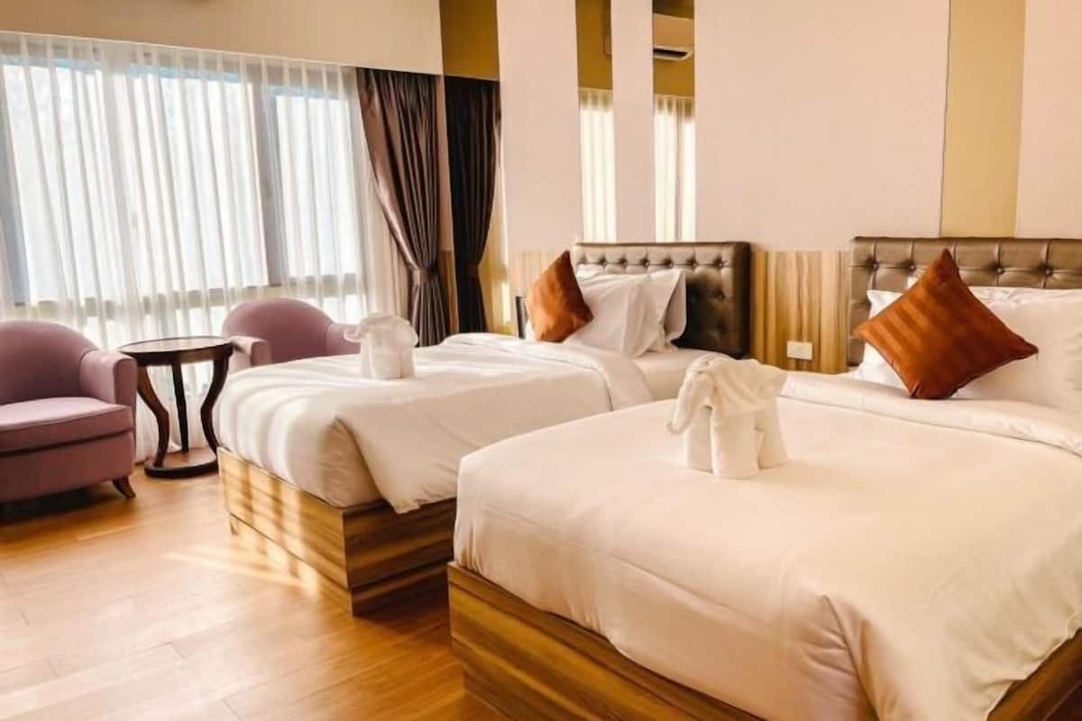 A hotel room with two beds, a small table, a chair, and a window with curtains.