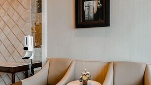 A modern lounge area with a cushioned bench, a small round table with a floral centerpiece, and a framed artwork on the wall.