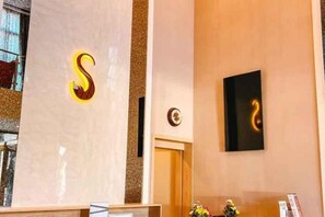 Ett välkomstområde med en receptionsdisk i marmor, en väggmonterad skylt med en stiliserad bokstav ”S” och ett inramat konstverk.