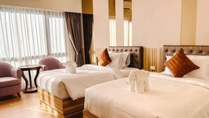 Une chambre d’hôtel avec deux lits, un coin salon comprenant un fauteuil, une petite table et une fenêtre avec des rideaux.