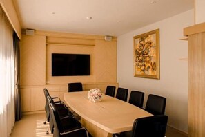 Un salón de conferencias con una larga mesa, sillas negras, un televisor de pantalla plana y un cuadro en la pared.
