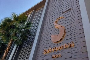 Un letrero de hotel con un gran logotipo en forma de 'S' y el nombre 'Sukruteha Hotel' en letras doradas sobre un revestimiento de ladrillo.
