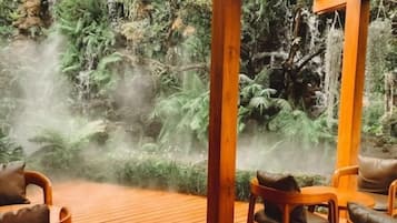 Terraza de madera con sillas que da a un jardín exuberante con cascada.