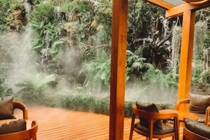 Terraza de madera con sillas que da a un jardín exuberante con cascada.